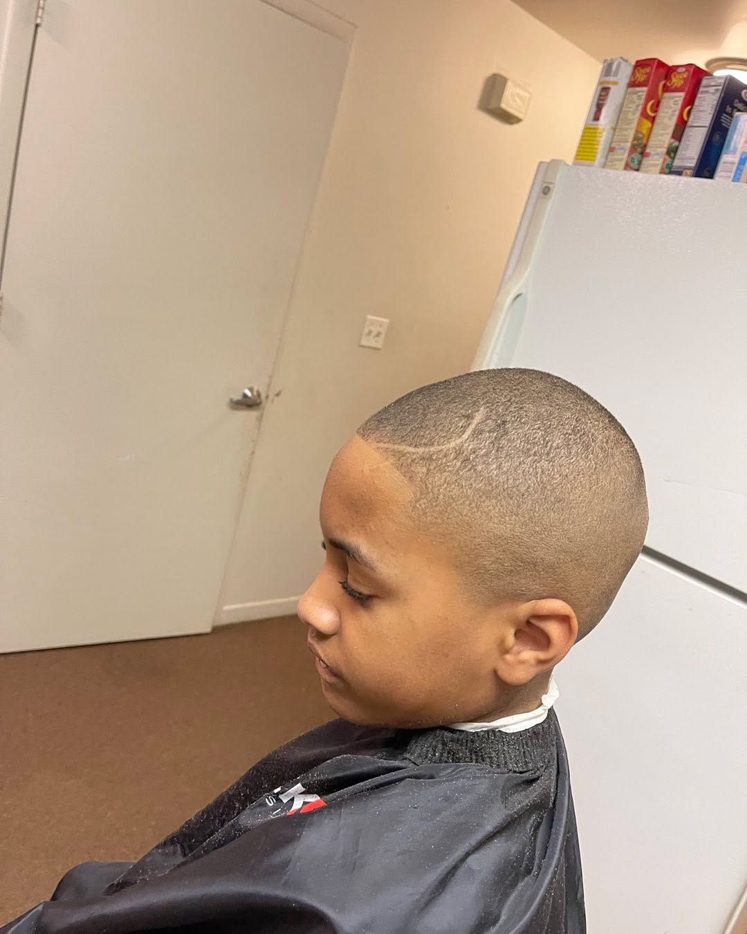 Kids buzz cut with a curved shaved design above the ear and a clean edge-up